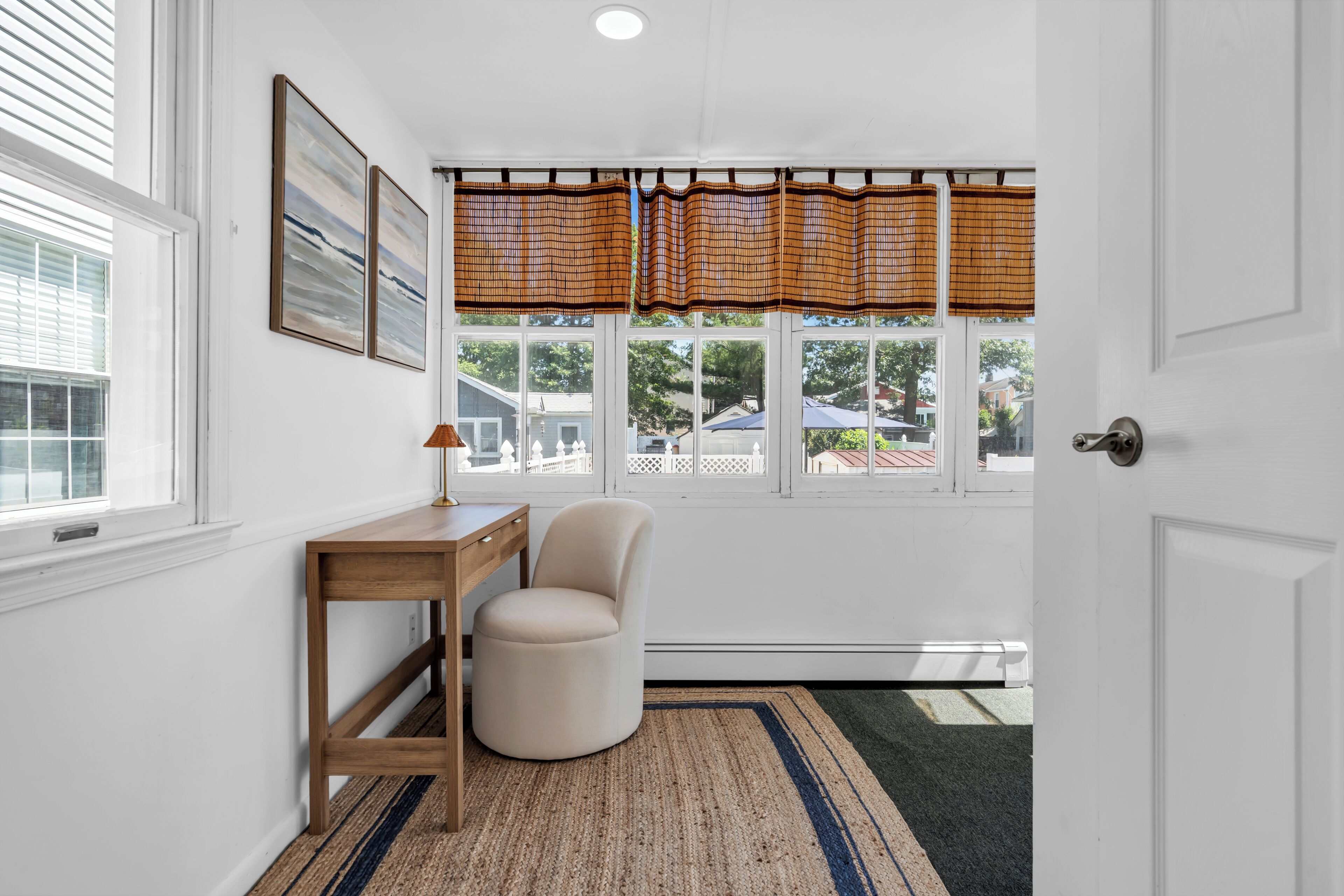 Habitación con escritorio, silla y ventanas amplias con persianas.