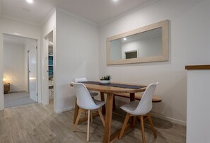 Un coin repas avec une table en bois, deux chaises blanches, un miroir au mur et une petite plante posée sur la table.