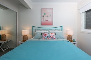 Un dormitorio con una cama, dos mesitas de noche, lámparas, un cuadro en la pared y una ventana con persianas.