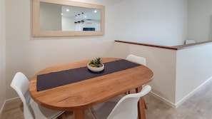Un comedor con una mesa de madera, sillas blancas, un mantel individual negro y una pequeña planta como centro de mesa.