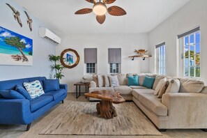 Ein Wohnzimmer mit einem blauen Sofa, beigen Couches, einem Holztisch und einem Deckenventilator.