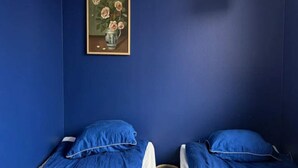 Una stanza con due letti, un piccolo sgabello, un quadro incorniciato e una lampada bianca.