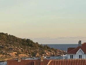 Uma casa à beira-mar com telhado de telhas vermelhas, paredes brancas e vista para o mar.