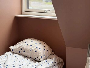 Quarto com janela, cama com roupa de cama listrada e mesa de cabeceira.