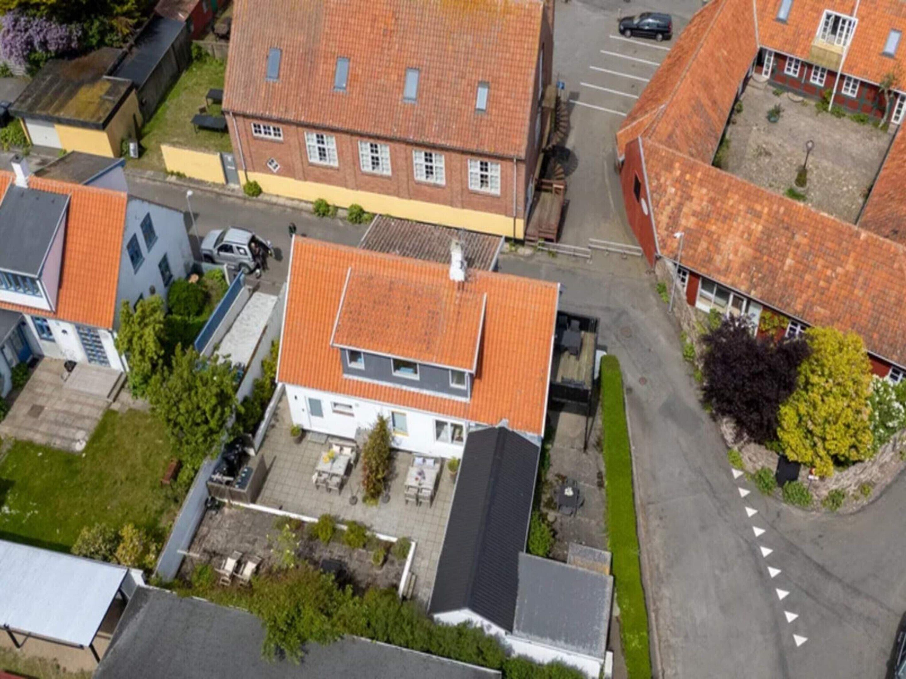 Vue aérienne d’un quartier résidentiel, avec une maison dotée d’un toit recouvert de tuiles rouges, d’un petit jardin et d’une allée pavée.