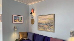 Una stanza con un divano viola, un poggiapiedi verde, un quadro incorniciato e una lampada a parete.