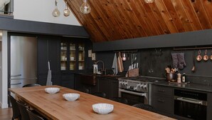 Eine moderne Küche mit Holztisch, schwarzen Schränken und hohen Decken.