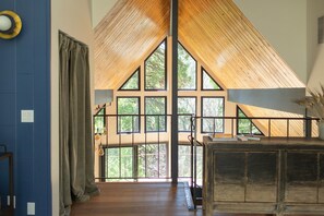 A spacious room with a high ceiling, large windows, and a wooden staircase. - Modern Cabin, European Design - 2 King Suites (Lake Arrowhead)