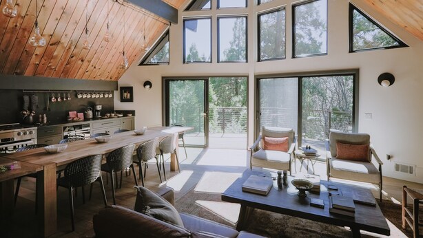Eine geräumige Küche mit modernen Geräten, ein Essbereich mit Holztisch und -stühlen sowie große Fenster mit Blick ins Freie.