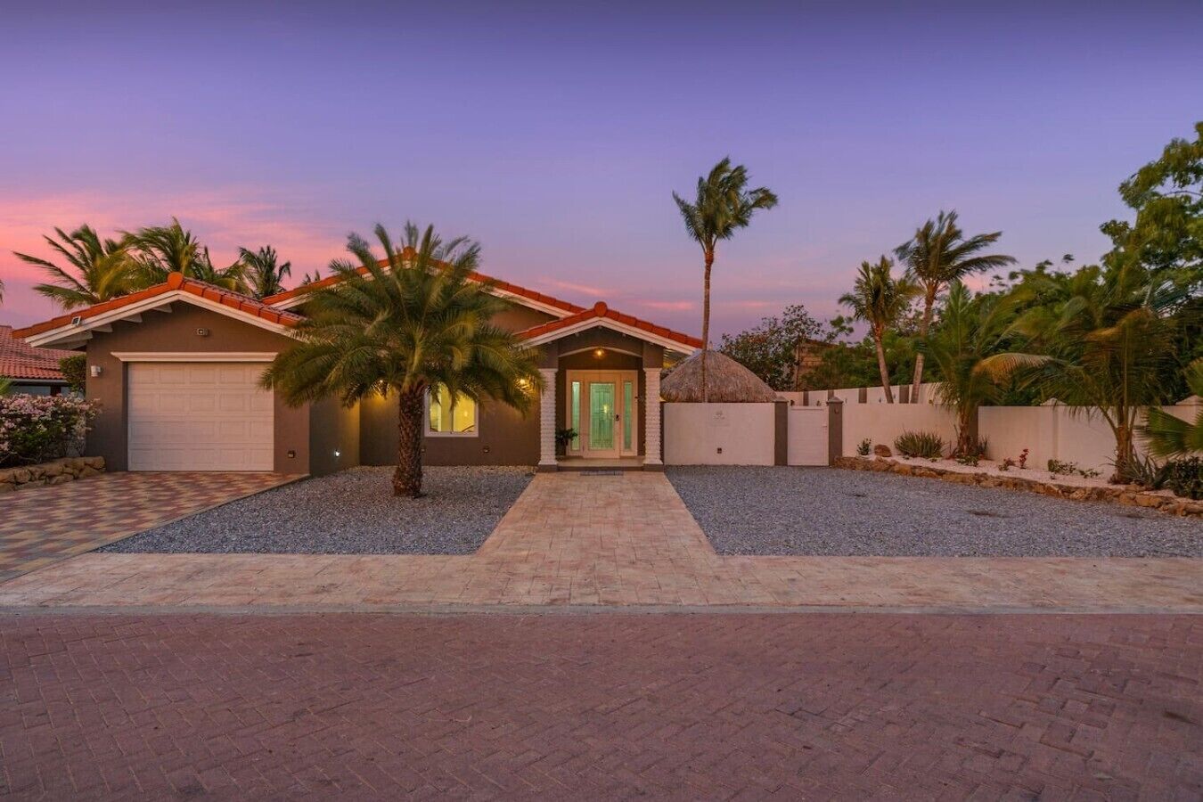 A residential house with a garage, a driveway, and a well-maintained lawn with palm trees.