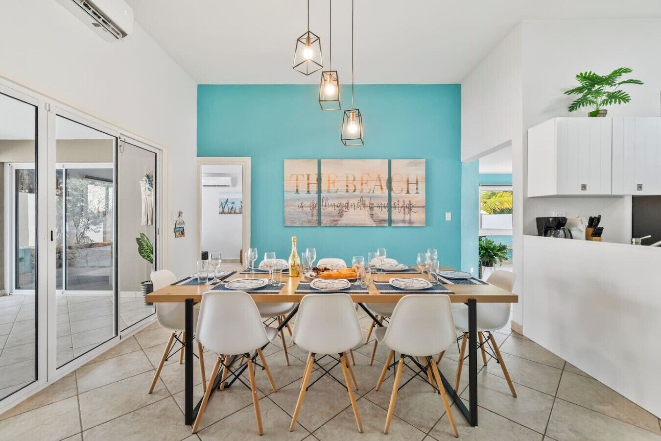 Un espace repas moderne avec un mur d’accent de couleur turquoise, un grand tableau et une cuisine aux meubles blancs.
