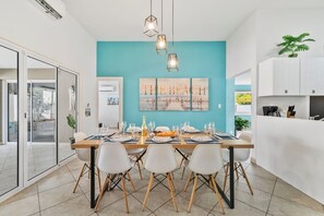 Un espace repas moderne avec un mur d’accent de couleur turquoise, un grand tableau et une cuisine aux meubles blancs.