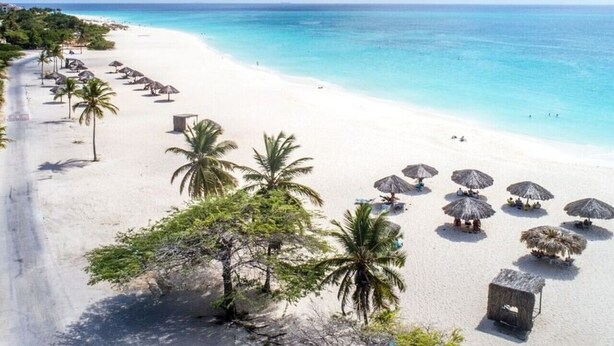 Une plage de sable blanc, avec une eau turquoise cristalline et des palmiers.