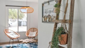 Une pièce comprenant deux fauteuils en osier, un luminaire suspendu, une étagère fixée au mur ornée de coquillages et un support vertical pour plantes.