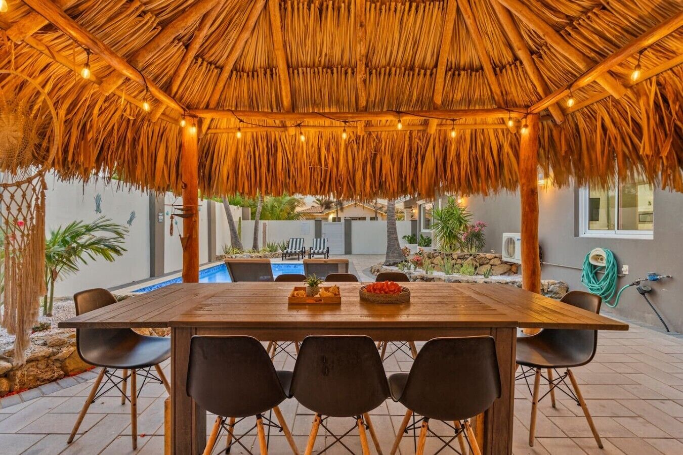Een terras buiten met rieten dak, een zwembad en een tuin.