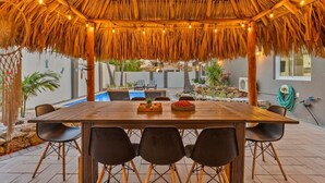 Un espace extérieur aménagé pour les repas, doté d’un toit de chaume, d’une piscine et d’un jardin.