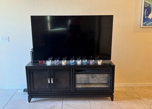 Un mueble multimedia negro con un televisor de pantalla plana, un aparador con puerta de vidrio y una fila de velas.