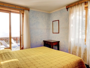 Una habitación con una cama, una mesita, un espejo y vistas a un balcón con sillas.