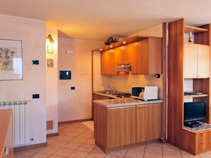 Una cocina compacta con armarios de madera, estufa, microondas y un pequeño comedor con una silla.