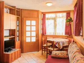 Una habitación acogedora con puerta de madera, televisor, una mesa de comedor con sillas y un sofá.