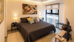 Ein modernes Schlafzimmer mit einem großen Bett, Nachttischlampen, einem Flachbildfernseher und einem Fenster mit Blick auf die Stadt.