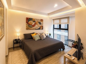 A modern bedroom with a large bed, bedside lamps, a flat-screen TV, and a window with a view of the city. - Mr. W | Cozy and Modern Loft at Torre Scala (Guadalajara)