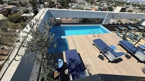 Ein Pool auf dem Dach mit Liegestühlen, umgeben von einer Stadtansicht.
