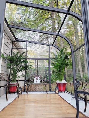 Eine überdachte Terrasse mit Holzboden, Metallgeländer und Blumentöpfen.