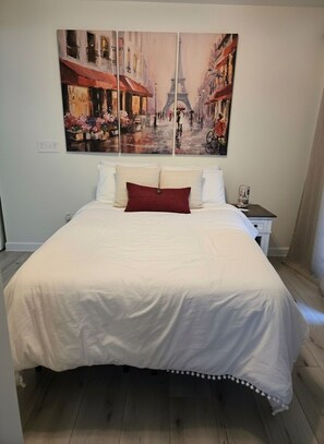 Une chambre à coucher avec un grand lit, une table de chevet et un tableau représentant une scÚne de rue.