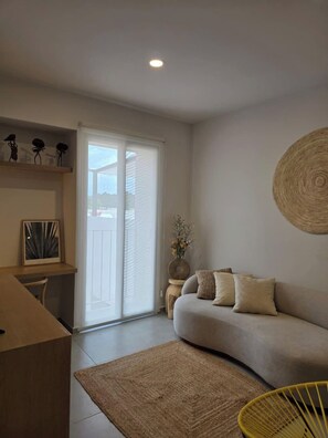 Una sala moderna con un sofá, una mesita de centro, una zona de comedor con una silla y un elemento decorativo en la pared.