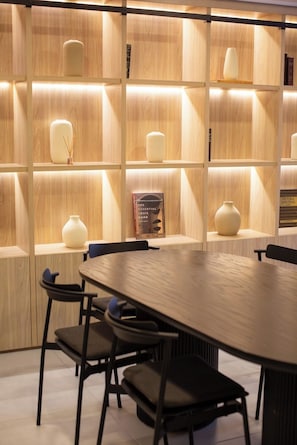 Ein moderner Essbereich mit einem Holztisch und Stühlen, beleuchteten Regalen mit Vasen sowie einem Buch mit dem Titel 'The Essential Louis Kahn'.