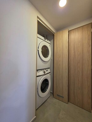Un cuarto de lavado con dos lavadoras y secadoras apiladas, puertas de madera y piso de baldosas.