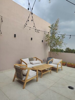Un patio con un conjunto de sofá de madera, una mesa, luces colgantes y una planta en maceta.