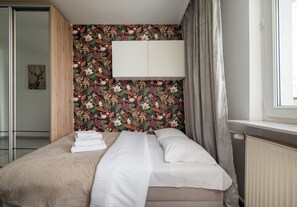 Ein Hotelzimmer mit einem Bett, einem weißen Kleiderschrank, blumigem Wandpapier und einem Fenster mit Vorhängen.