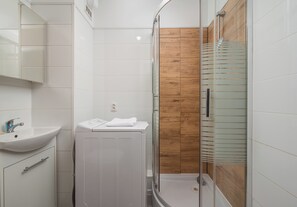Ein Badezimmer mit Waschbecken, Spiegel, Dusche und einer Wand aus Holzpaneelen.