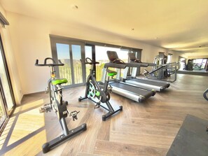 Ein Fitnessraum mit Trainingsgeräten, großen Fenstern und Holzboden.
