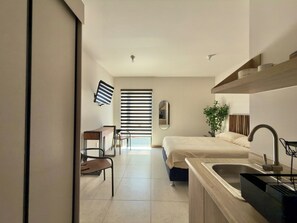 Ein modernes Hotelzimmer mit Bett, Schreibtisch, Stuhl, Waschbecken und einem großen Fenster mit Jalousien.