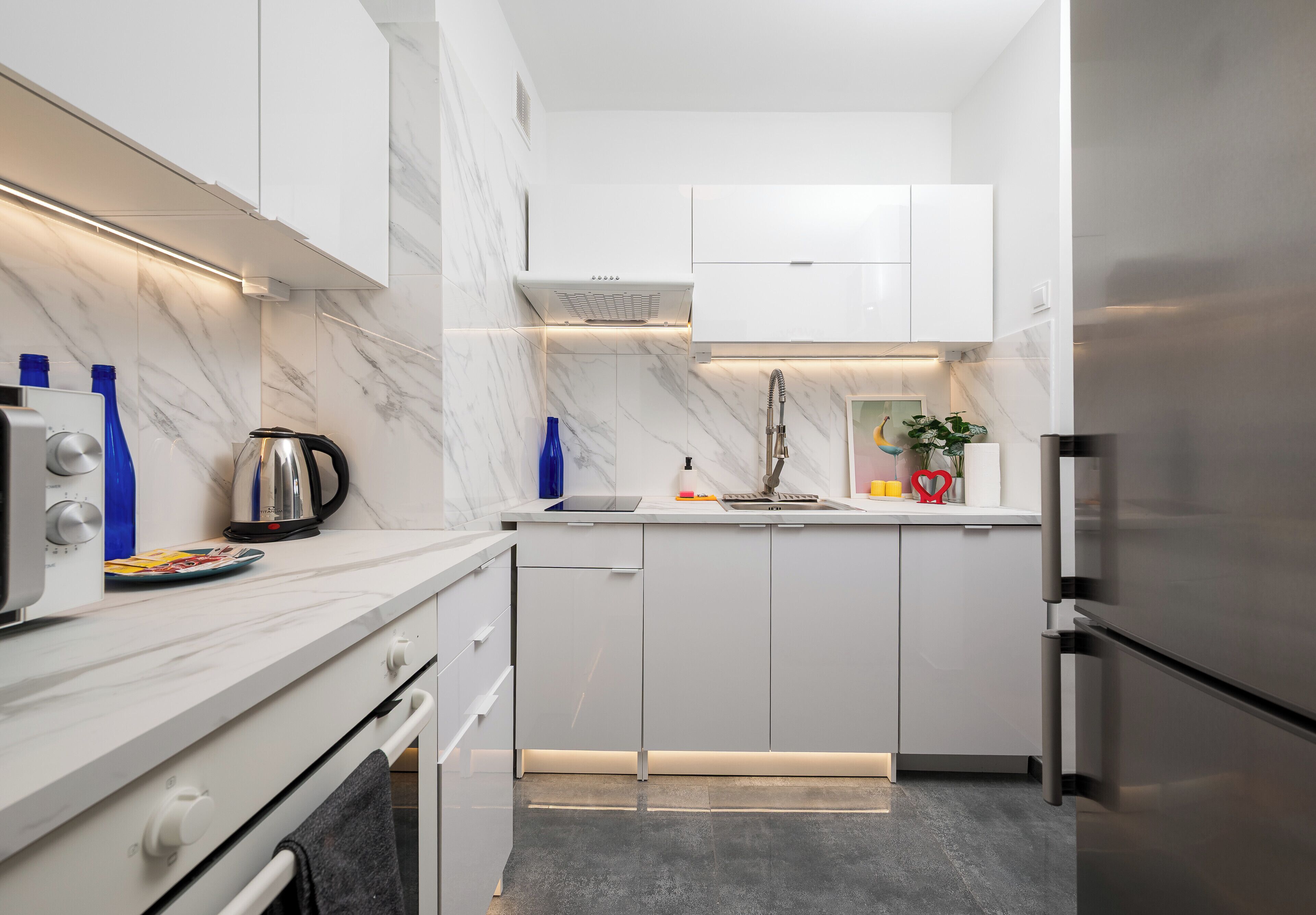 A modern kitchen with white cabinets, a stainless steel refrigerator, and a marble backsplash.