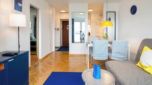 A modern living room with a sofa, a dining table with chairs, a lamp, and a desk with a chair. - Warszawa Wola Cozy Apartment (Warszawa)