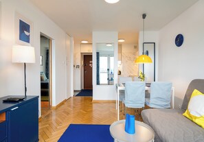 Ein modernes Wohnzimmer mit einer Couch, einem Esstisch mit Stühlen, einer Lampe und einem Schreibtisch mit Sessel.