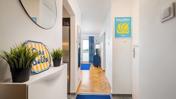 A hallway with a blue carpet, potted plants, a mirror, and a sign for Mallorca Spain. - Warszawa Wola Cozy Apartment (Warszawa)
