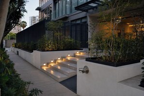 Ein modernes Gebäude mit einer Treppe zu einem verschlossenen Eingang, umgeben von Grünflächen und einem Weg.