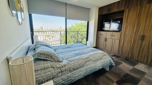 Une chambre avec une grande fenêtre, un lit, une télévision et une armoire en bois.