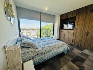 A bedroom with a large window, a bed, a TV, and a wooden cabinet. - Stylish 2BR Apartment at Torre Bermeo (Zapopan)
