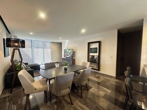 Un espace repas moderne avec une table rectangulaire, six chaises, un lampadaire, un téléviseur et un tableau encadré au mur.