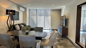 Un salon moderne comprenant un coin repas, un téléviseur à écran plat et une grande fenêtre équipée de stores.