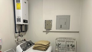 Une buanderie équipée d’un lave-linge, d’un sèche-linge, ainsi qu’une pièce technique avec un thermostat et un tableau électrique.
