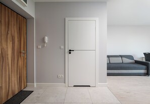 A modern room with a wooden wardrobe, a white door, a grey sofa, and a small table with a lamp. - Warszawa Rakowska Smart Studio (Warszawa)