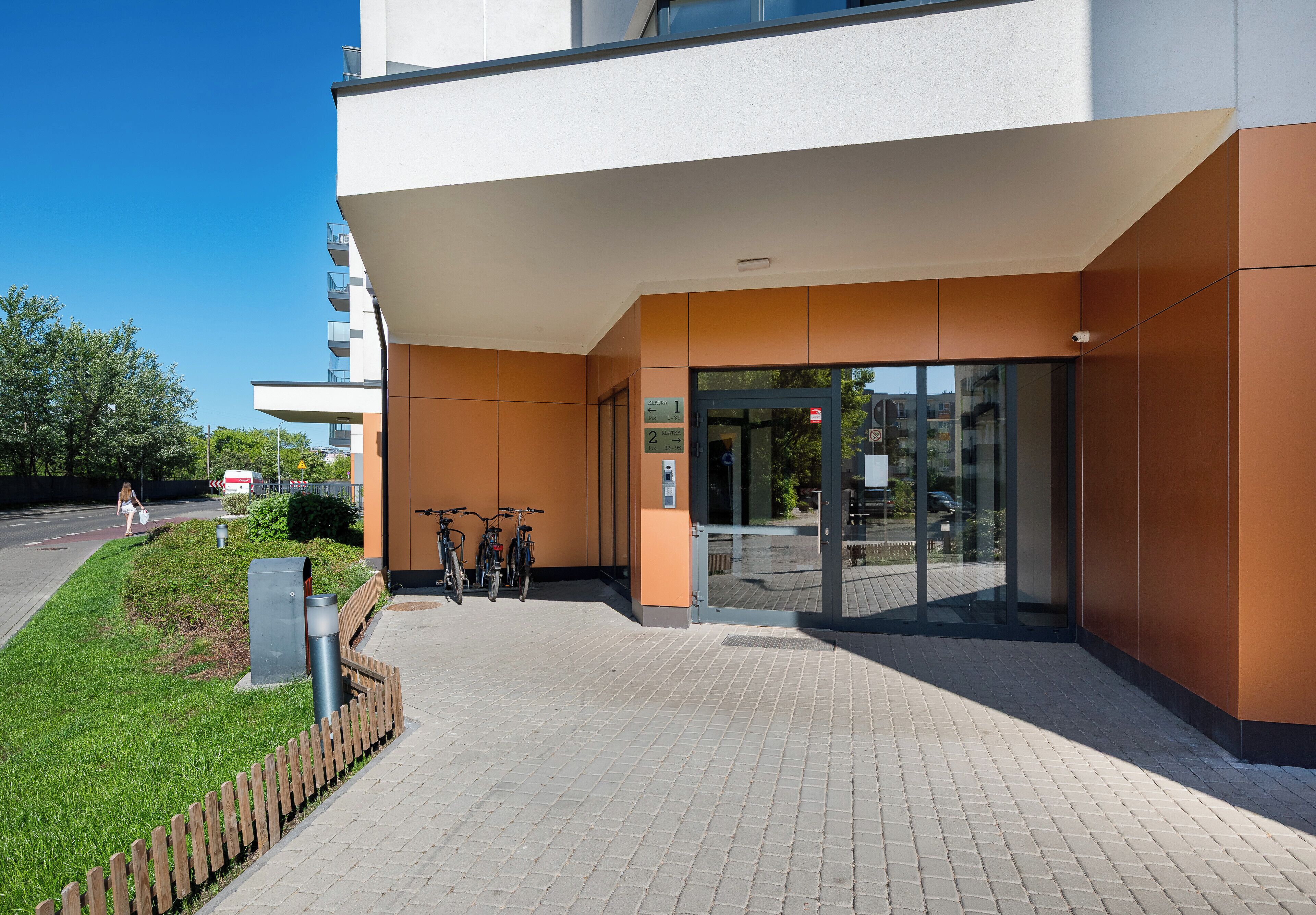 A modern building entrance with a glass door, a bike rack, and a paved walkway.