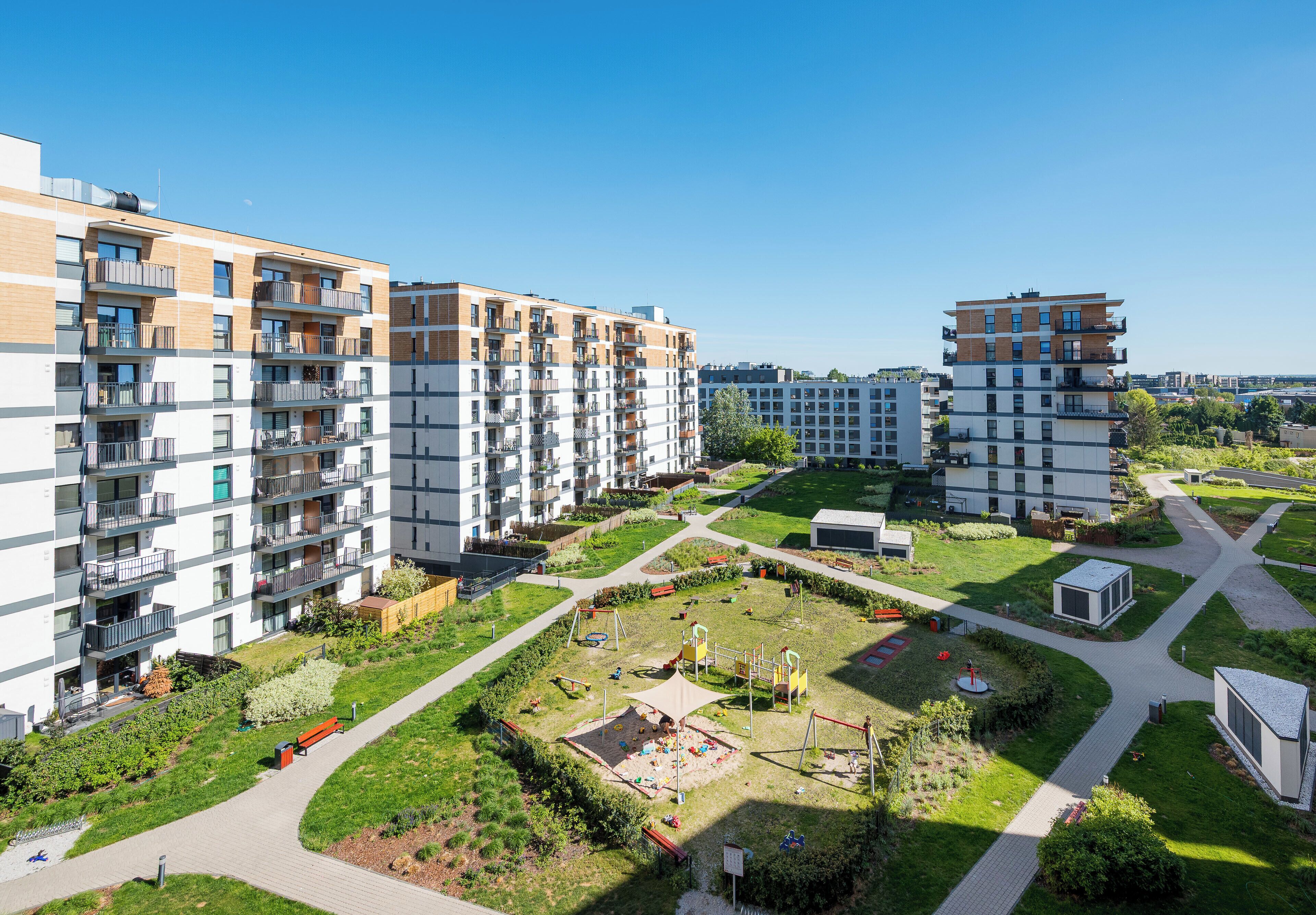 Un ensemble résidentiel comprenant plusieurs immeubles d’appartements, une cour centrale avec des jeux pour enfants et un espace vert bien entretenu.